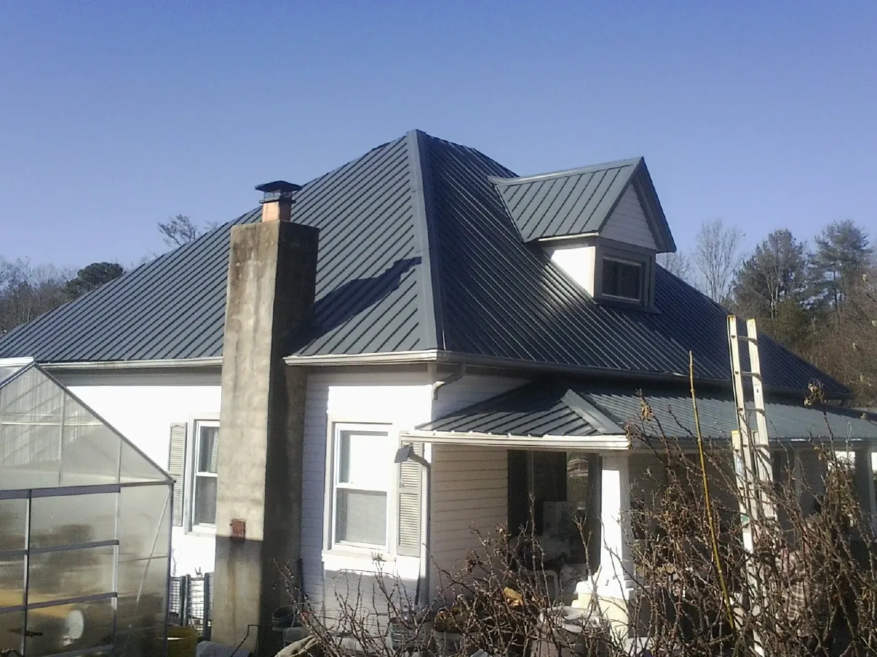 Dark blue standing seam metal roof on a white farmhouse with dormer — Slate & Tile Roof Repair by Roofing Brothers in Lomira