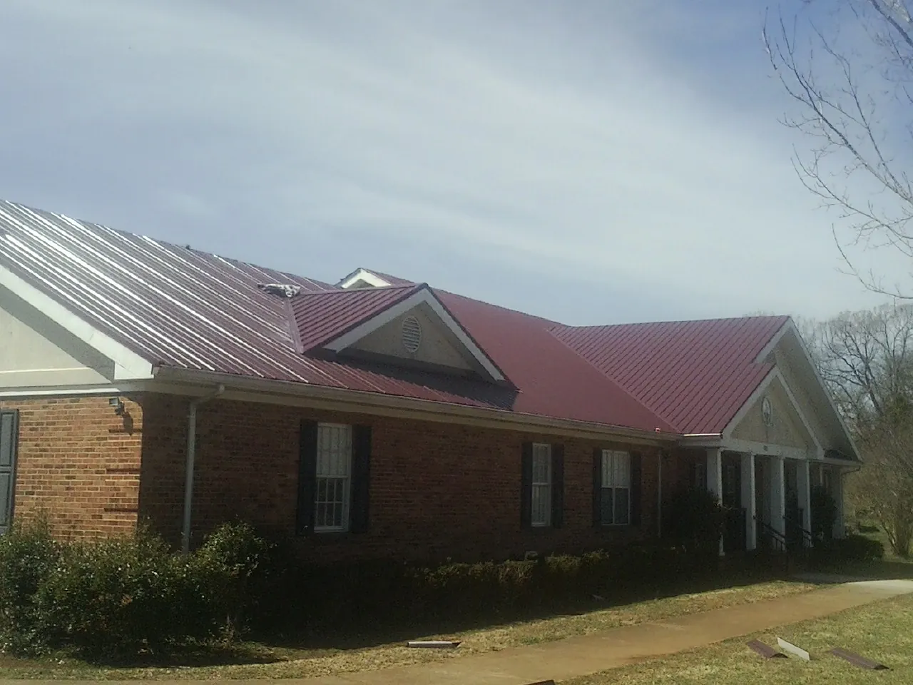 Red metal roof with gabled entries on a long brick building, from a Hail Damage Roof Repair job in Lomira