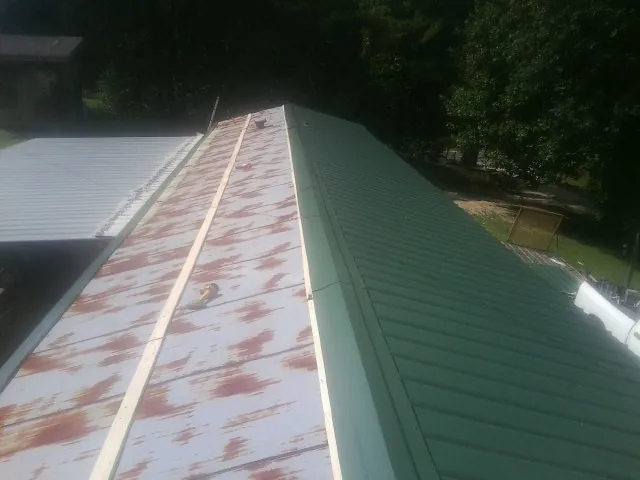 Old rusted panels beside newly installed green metal roofing — Wind Damage Roof Repair by Roofing Brothers in Lomira