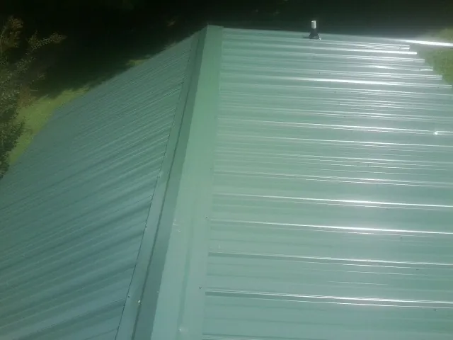 New green metal panels meeting at the ridge of a roof — Flat Roof Repair work by our crew in Lomira
