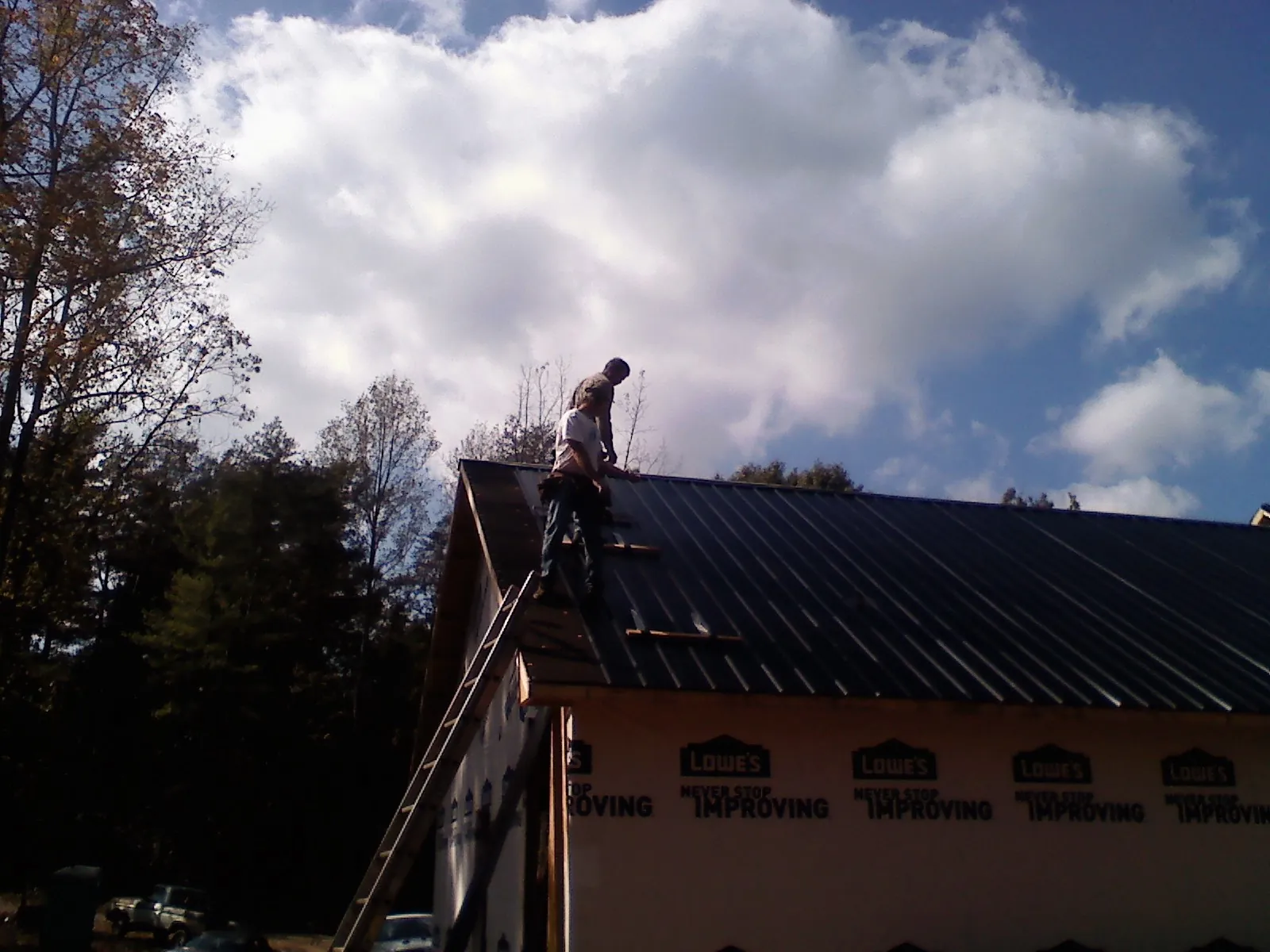 Roofer fastening dark metal panels high against a cloudy sky, from a Roof Inspection job in Lomira
