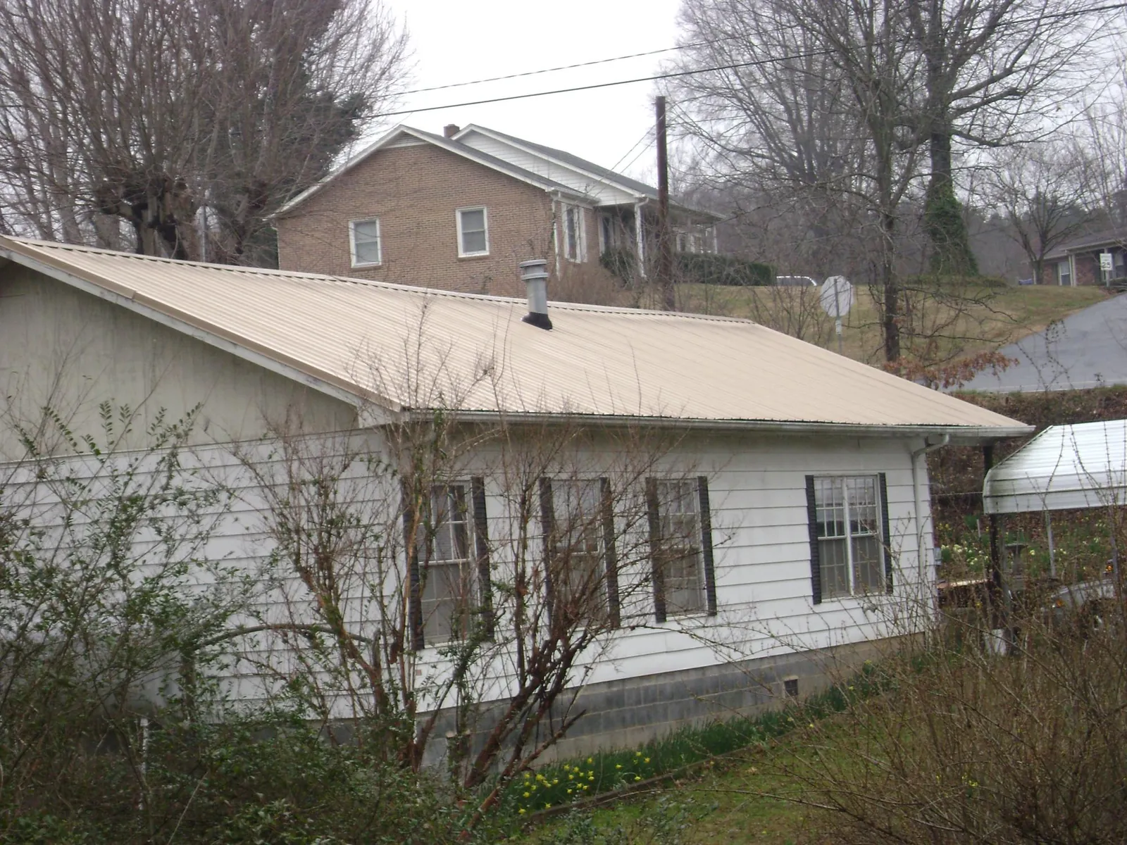 Tan metal roof on a white sided house set into a hillside — Commercial Roofing by Roofing Brothers in Lomira